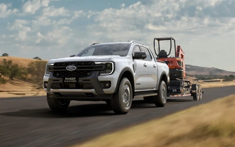 Ford Ranger Hybrid towing a boat with the family pictured near a river.